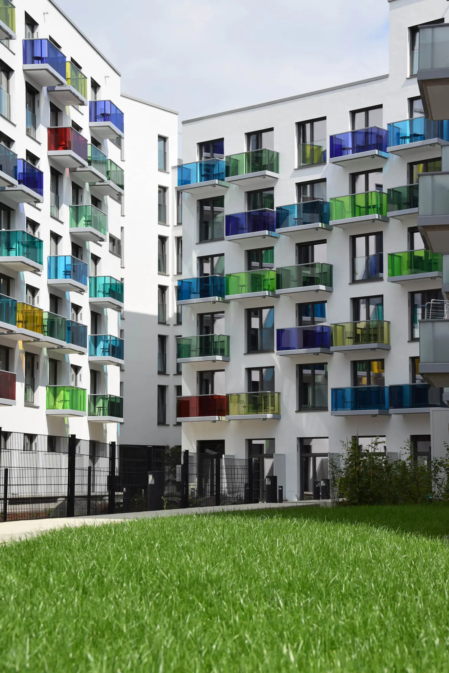 Fassade mit bunten Glasbalkonen und Rasenfläche davor